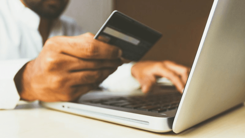 Persona con carta di credito in mano davanti a un laptop durante un acquisto online