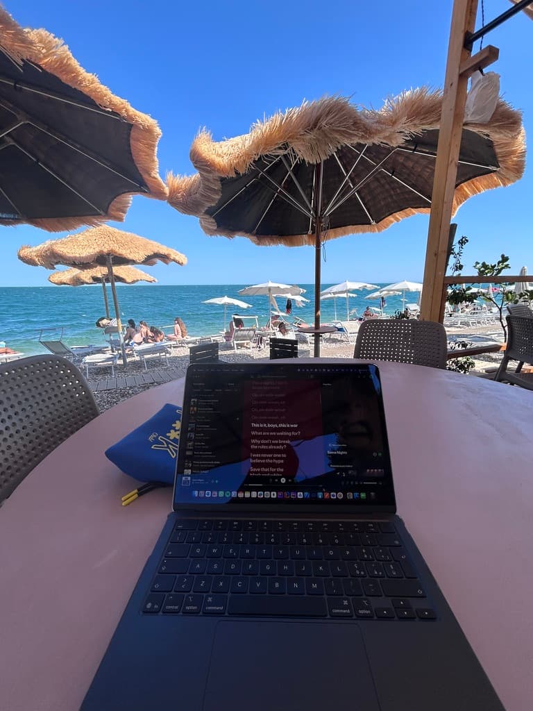 Mobile engineer che lavora da remoto su un MacBook presso un beach club italiano con vista mare, stile di vita flessibile